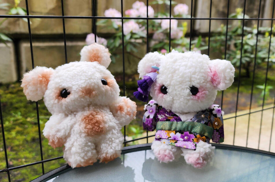 Handmade plush dolls. The left one is white with brown blush, waving its paw. The right one is white with pink blush, wearing a purple kimono.